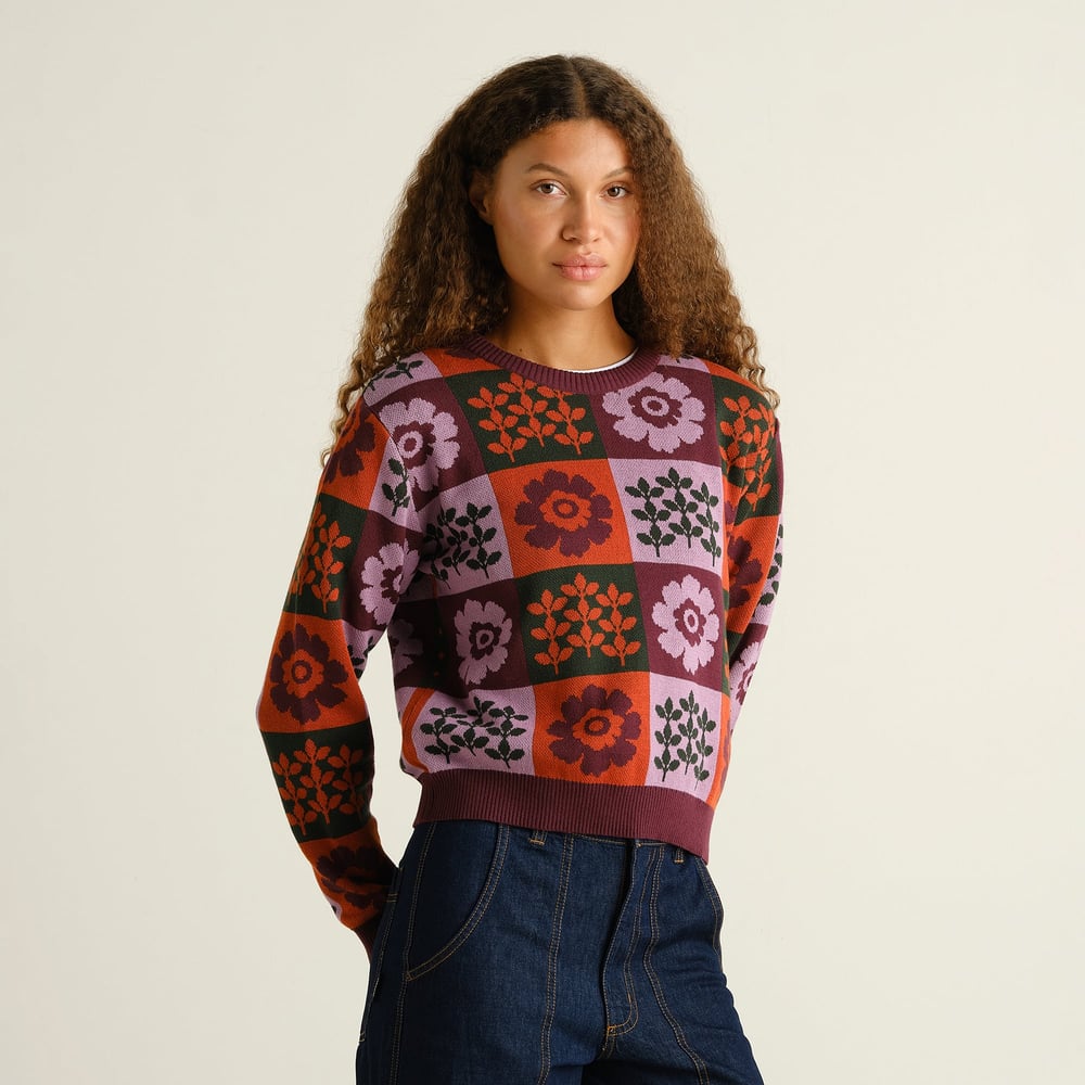 Model wears the Arendal Nature Check sweater, a cozy jacquard knit with a multi-colored floral and leaf checkerboard pattern.