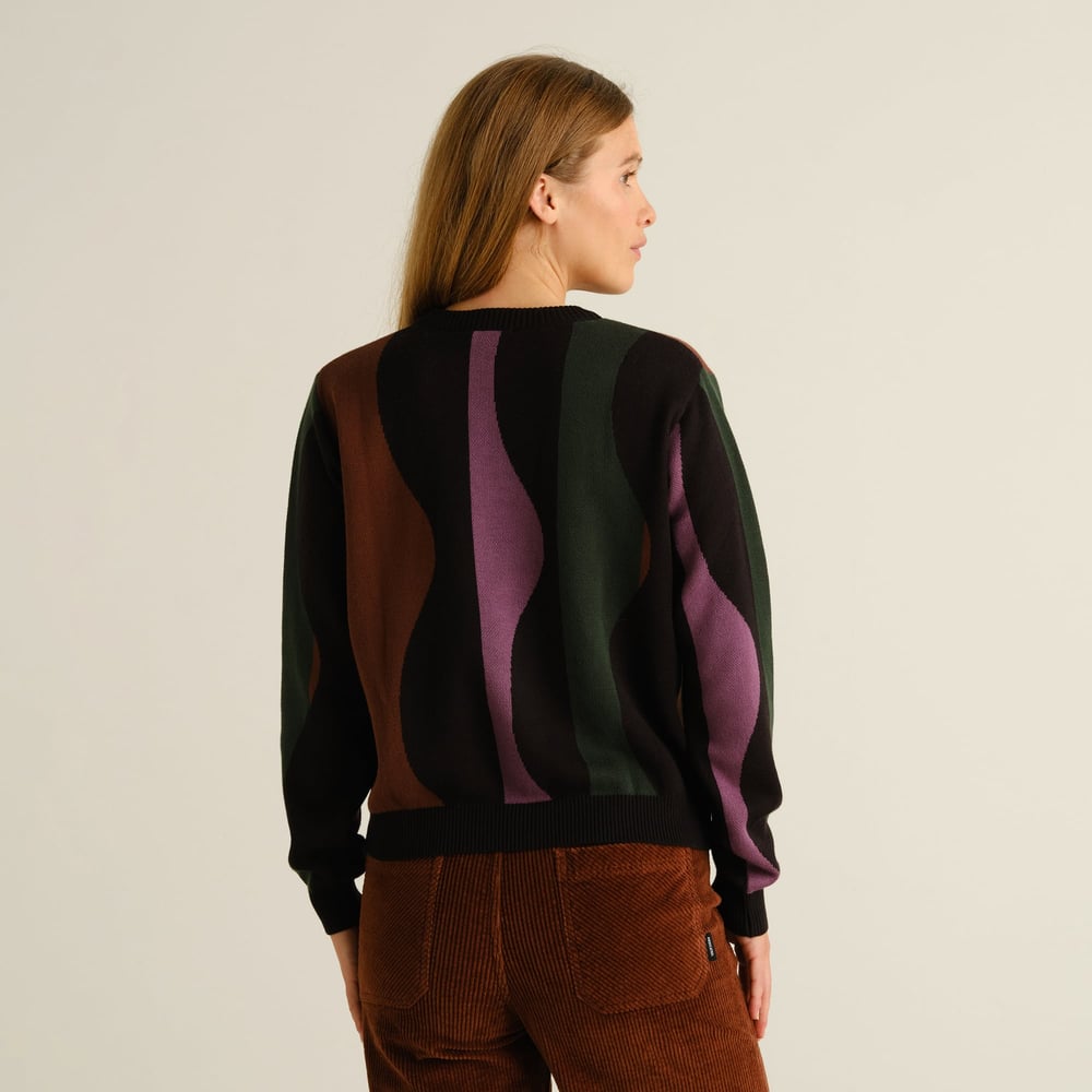 A model, seen from the back, wears the Sweater Arendal in a multi-color wavy stripe pattern with brown corduroy pants.