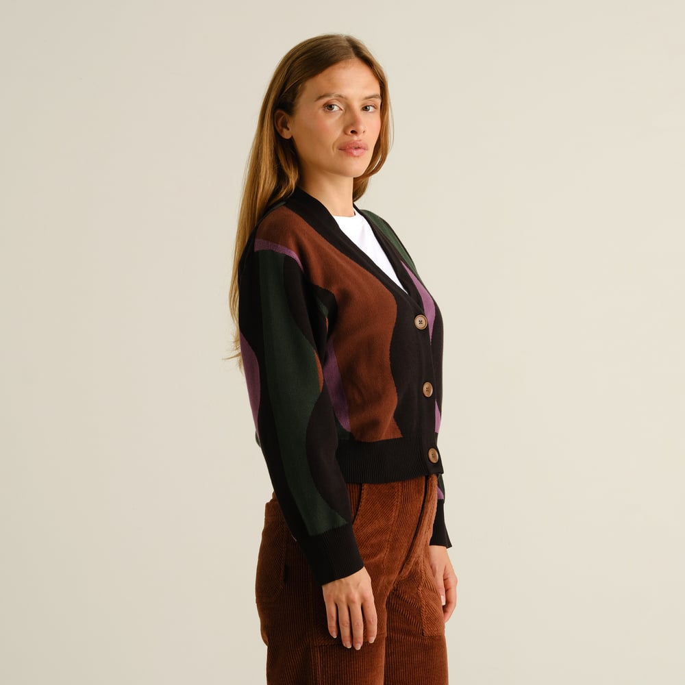 Side view of a woman wearing the multi-colored Kanan Wavy Stripe cardigan with brown corduroy trousers.