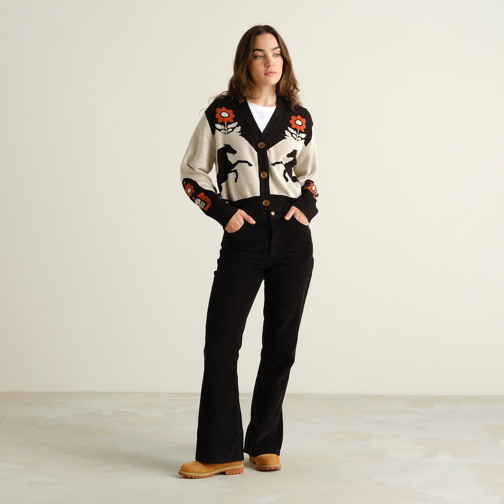 Full length shot of a woman wearing the Kanan Western Multi Color cardigan, paired with black flared trousers and tan boots.
