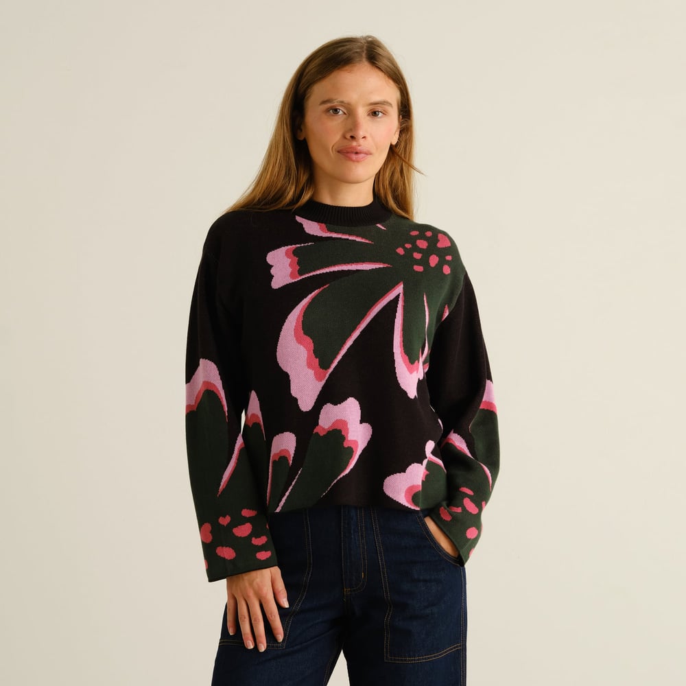 A model wears the Sweater Limhamn Big Bloom, a black jacquard knit with a bold floral pattern in pink and dark green.