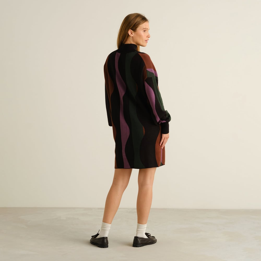 Model from the back wearing the Nikkala dress with a wavy multi-color stripe pattern, styled with loafers and white socks.