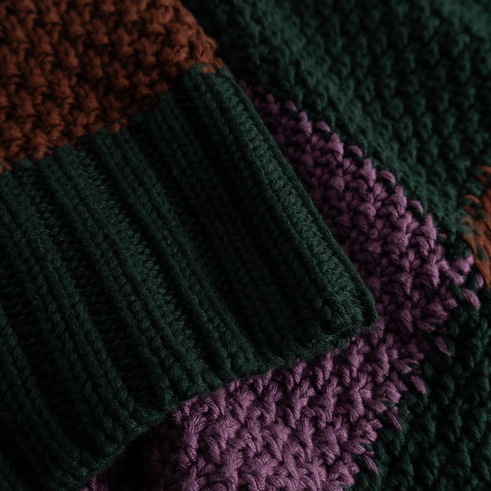 A detailed close-up of the chunky, multi-colored knit of the Gotland sweater, focusing on the dark green ribbed cuff.