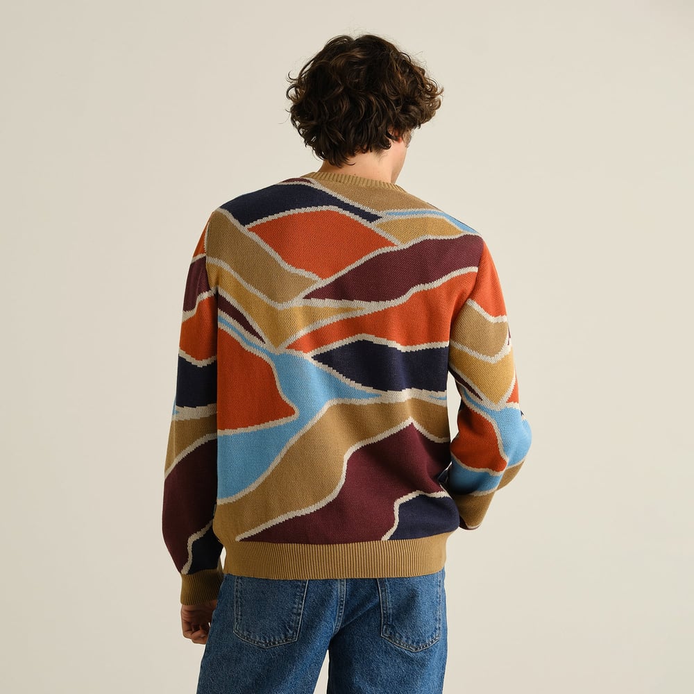 Model seen from behind wearing the Sweater Mora Patch Valley, showing off its colorful and abstract jacquard knit pattern.