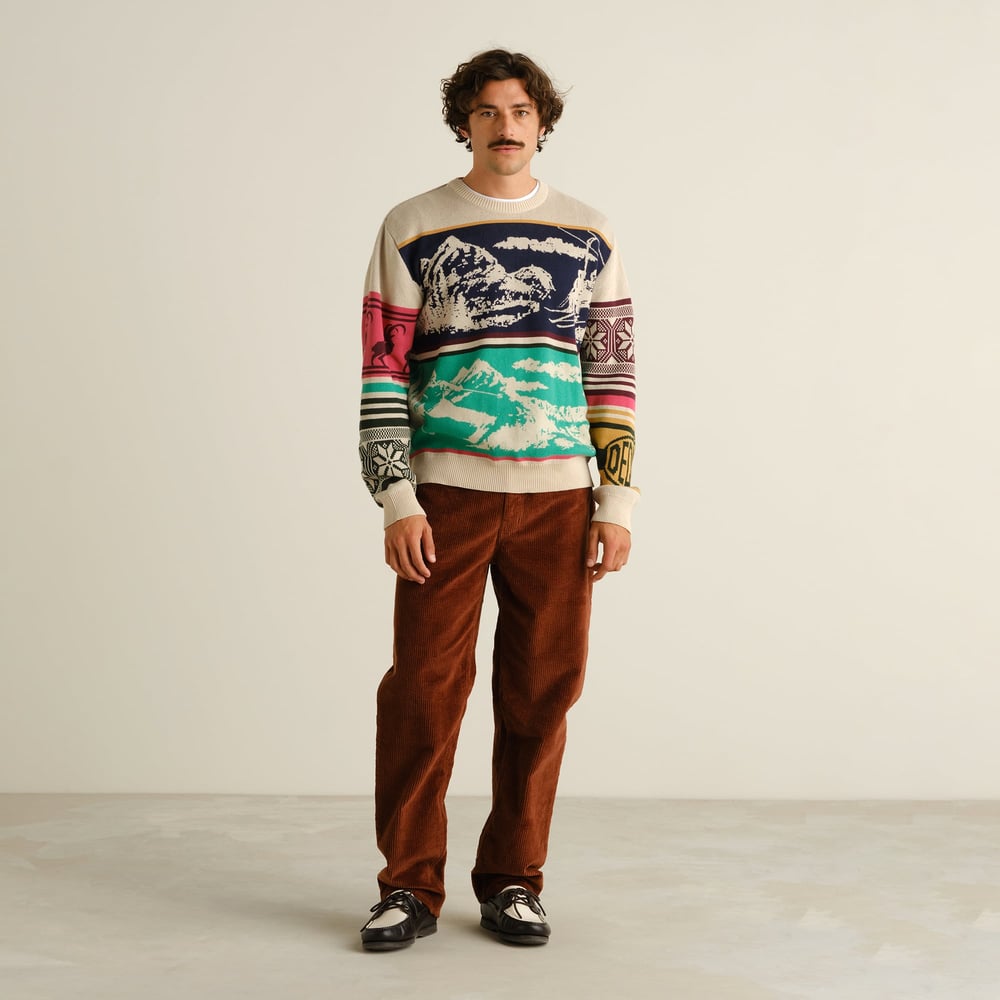 Male model in a full-length shot wearing the multi-colored Mora Retro Ski Blocks sweater with brown corduroy trousers.