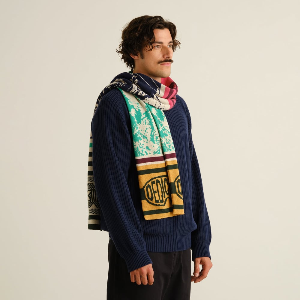 Male model in a studio setting, wearing a navy blue sweater and the vibrant, multi-colored Rossberga Retro Ski scarf.