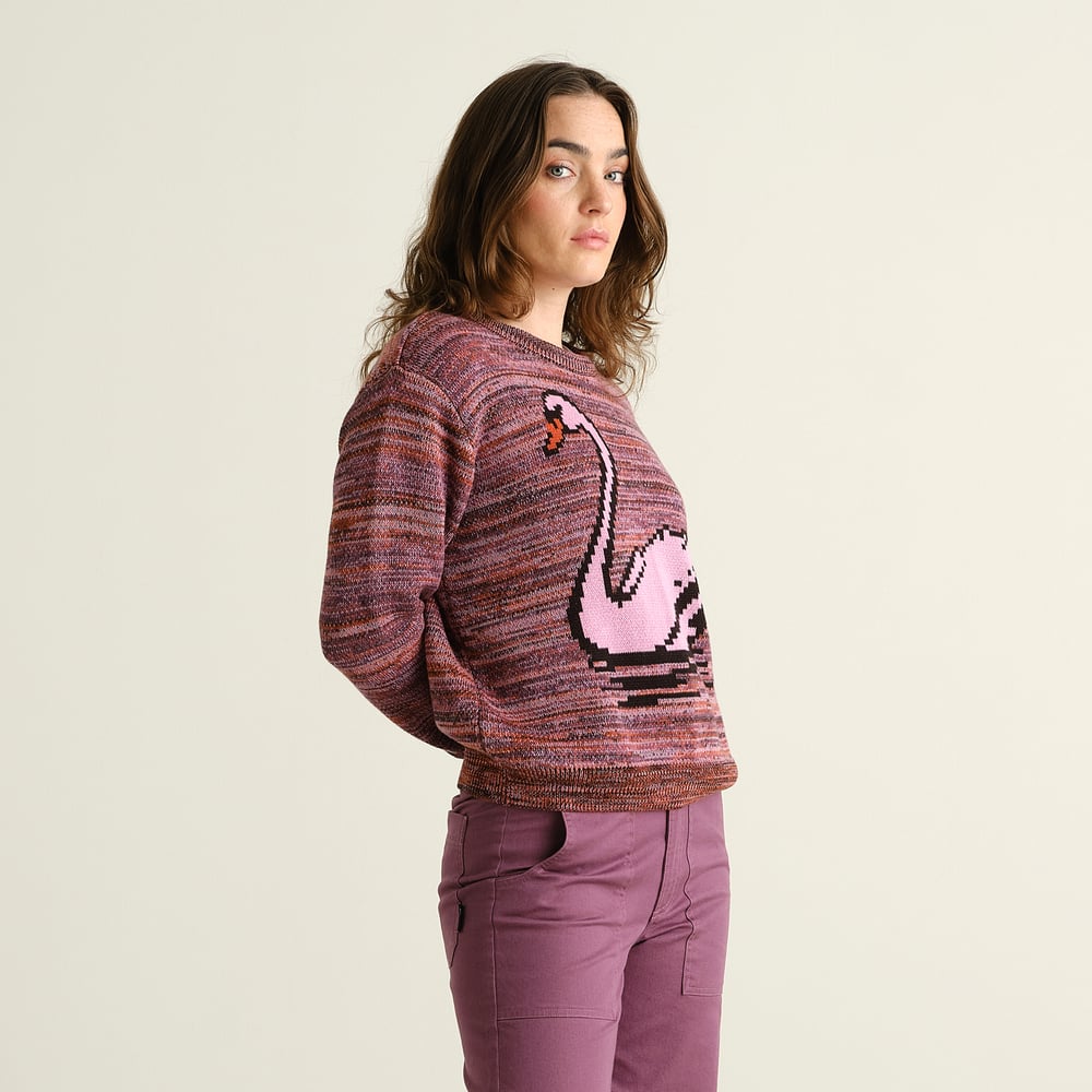 A woman looks over her shoulder, showing off the fun pixelated swan design on the multi-colored Arendal knit sweater.