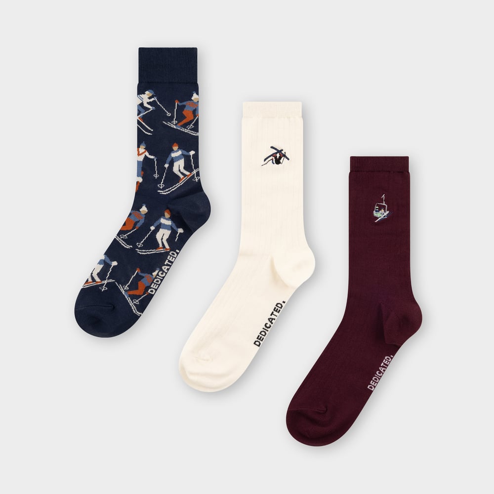 Flat lay av Socks Ski 3-pack: marinblått skidåkarmönster, cremefärgad med en skidåkare och en vinröd med skidlift.