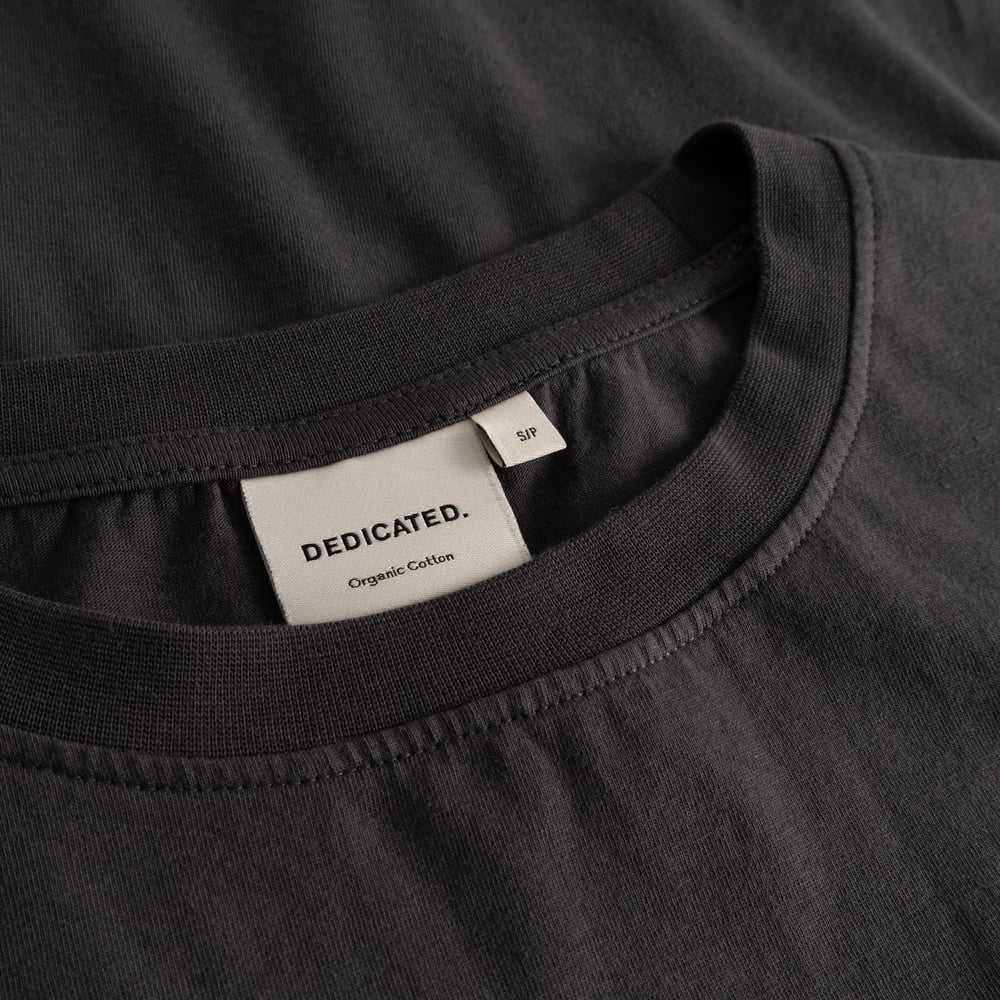 Detail shot of the Dedicated brand label inside the soft, ribbed collar of the charcoal T-shirt Vadstena.