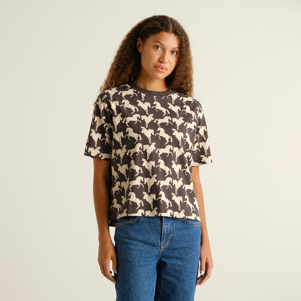 Model wears the relaxed-fit Vadstena T-shirt in charcoal, featuring an all-over wild horses print, with blue jeans.
