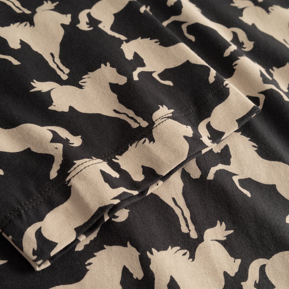 Close-up of the sleeve on the T-shirt Vadstena, showing the all-over wild horses print on charcoal fabric.