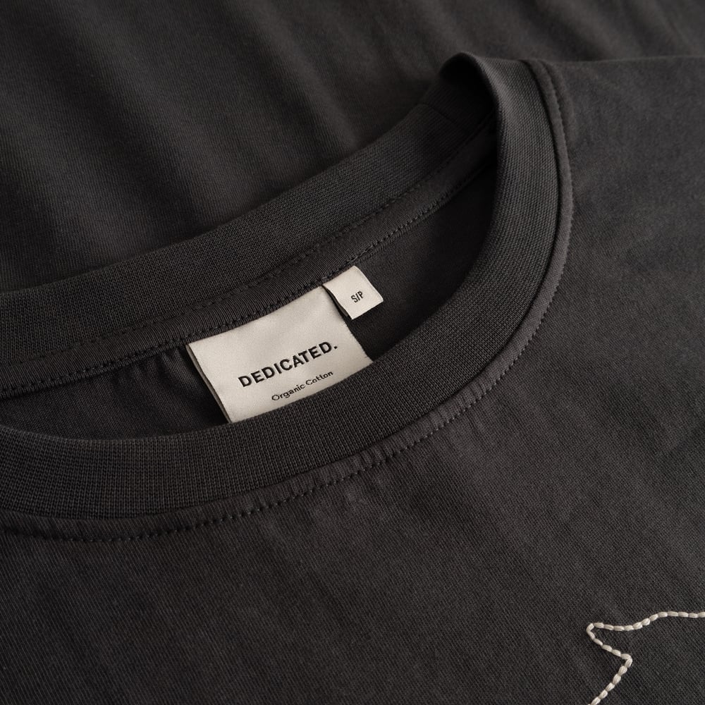 Detailed close-up of the charcoal T-shirt Vadstena's neckline, showing the Dedicated brand label and ribbed collar.