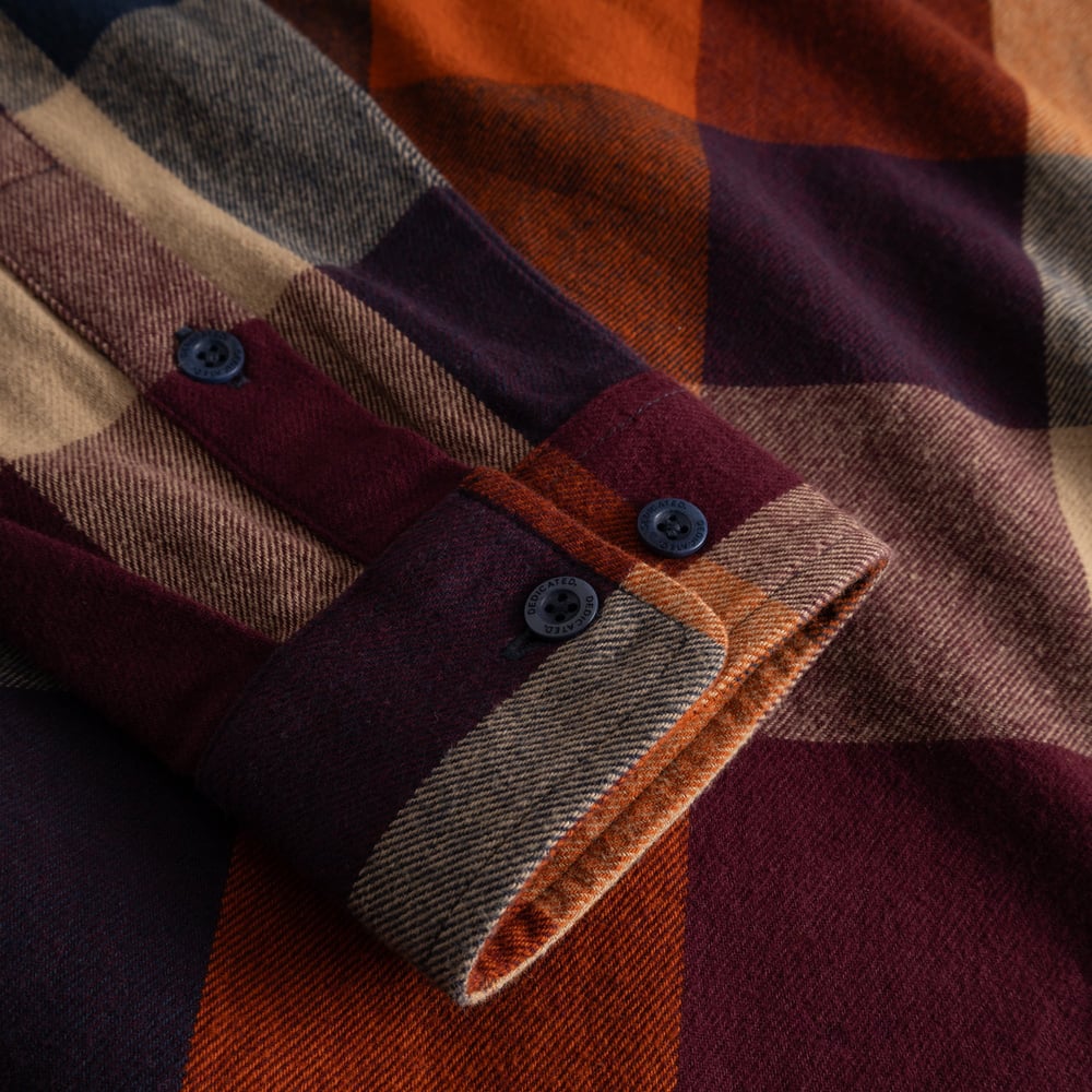 A close-up of the soft flannel cuff of the Rute shirt, featuring a muted plaid pattern and custom branded buttons.