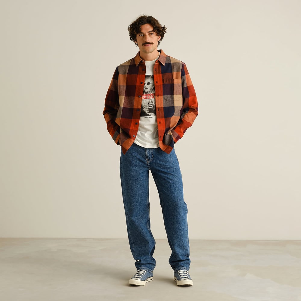 Model wears the Rute Flannel Shirt in muted multi-color, styled open over a graphic tee with relaxed fit blue jeans.