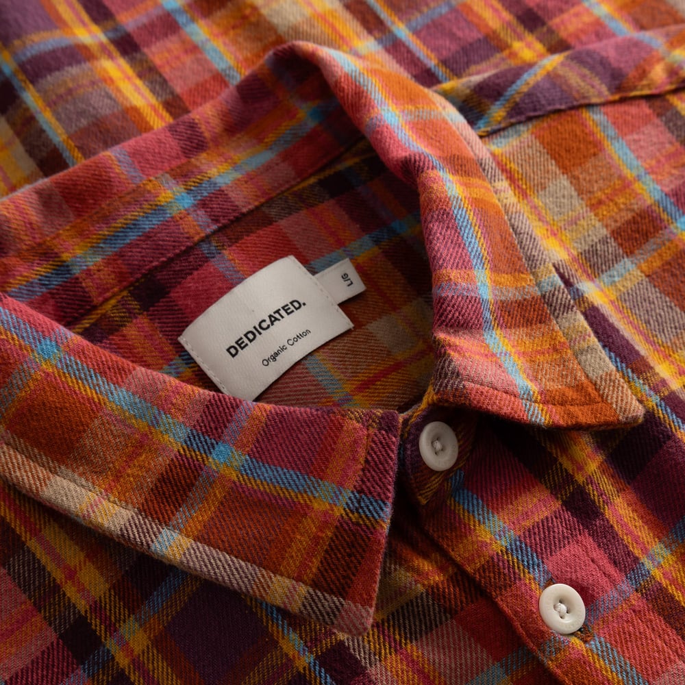 A detailed close-up of the Rute Shirt's collar in a warm madras check flannel, showing the Dedicated brand label.