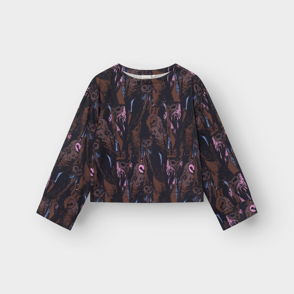 A flat-lay photo of the Top Udda, showing its boxy fit, wide sleeves, and expressive multi-color owl print.