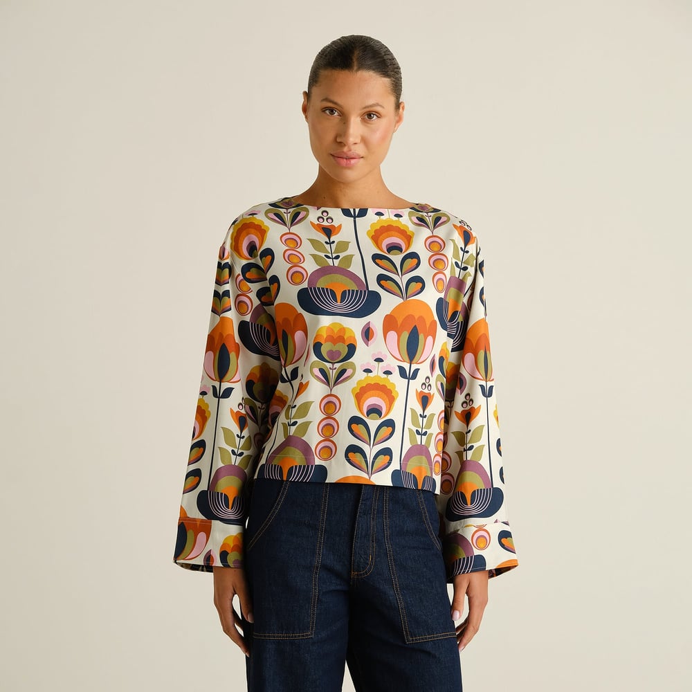 A model wears the modern, boxy Top Udda in a colorful Autumn Harvest print, featuring a boat neckline and wide sleeves.
