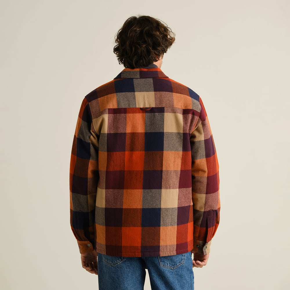 Back view of a male model wearing the muted multi-color Jacket Torp Flannel Check over blue jeans in a studio setting.