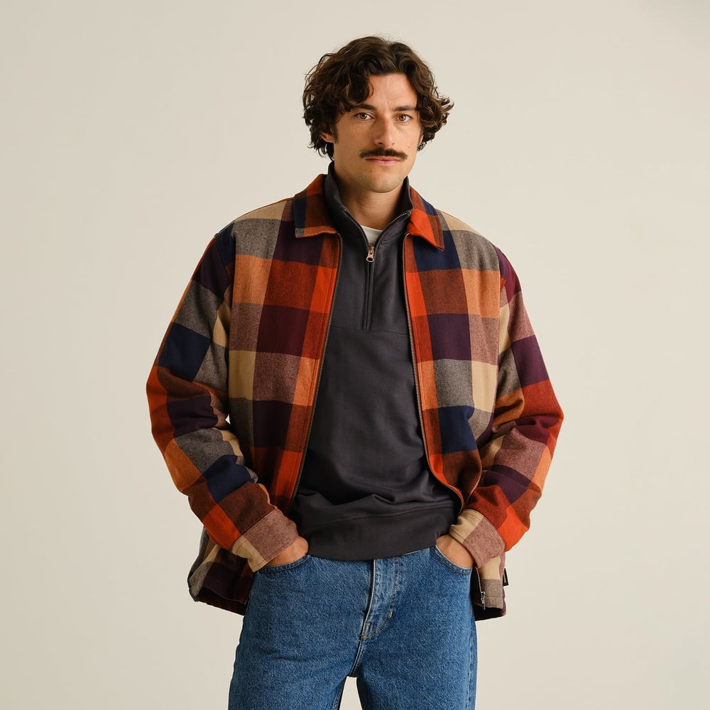 Man models the Torp Flannel Check Jacket in Muted Multi Color over a grey sweater and blue jeans.