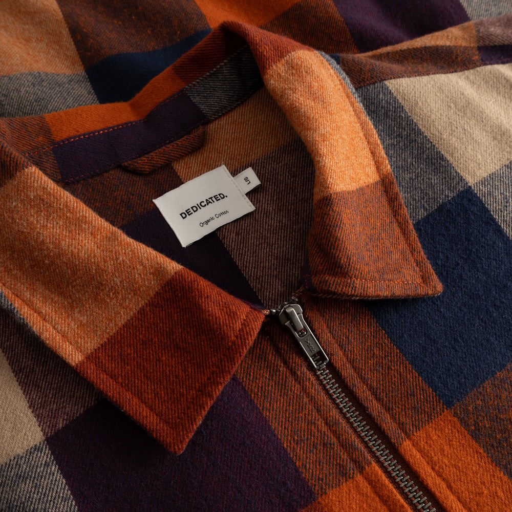 A detailed close-up of the Torp Flannel Check Jacket, showing the soft fabric, zipper, and the Dedicated brand label.