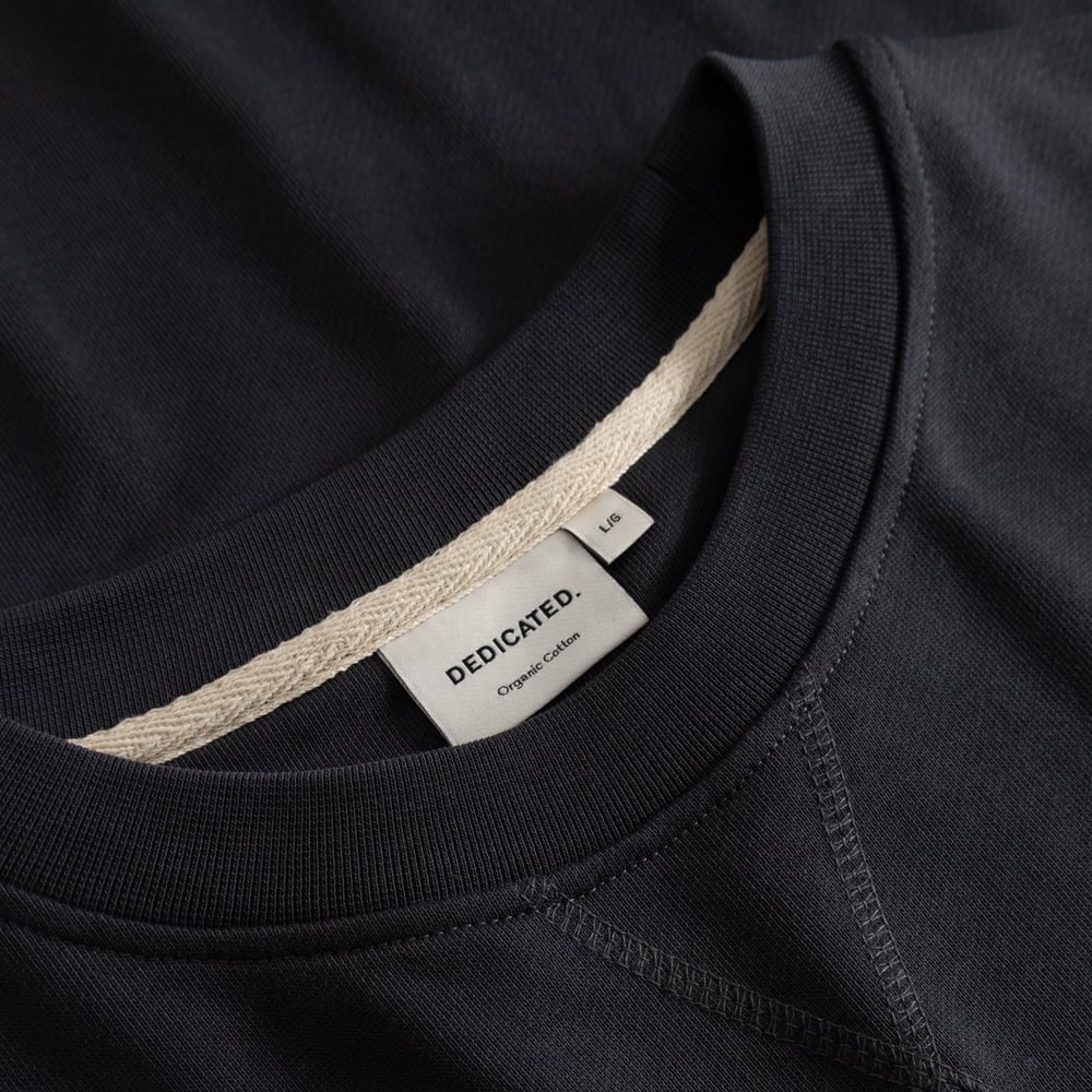 A close-up view of the Sweatshirt Bettna Phantom Black, highlighting the ribbed crew neck and classic Dedicated brand label.