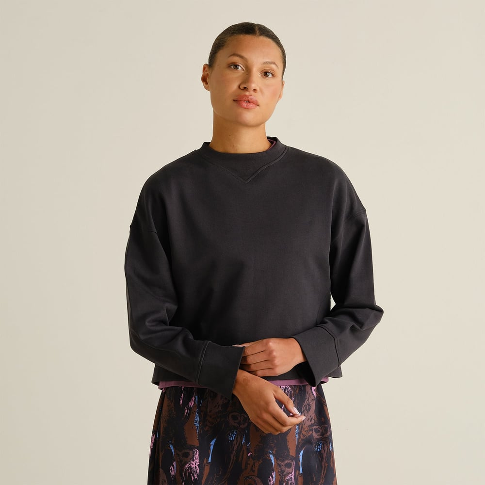 A model shows off the relaxed fit of the Sweatshirt Gia in Phantom Black, styled with a patterned skirt.