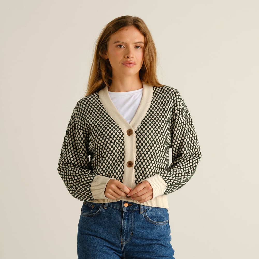Modell som bär den mörkgröna och vaniljvitt mönstrade koftan Kanan Bubble Knit tillsammans med jeans.