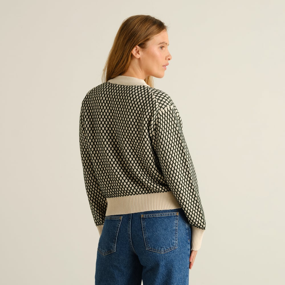 Kvinna sedd snett bakifrån i den mörkgröna och vaniljvita Kanan Bubble Knit Cardigan, stylad med blåjeans.