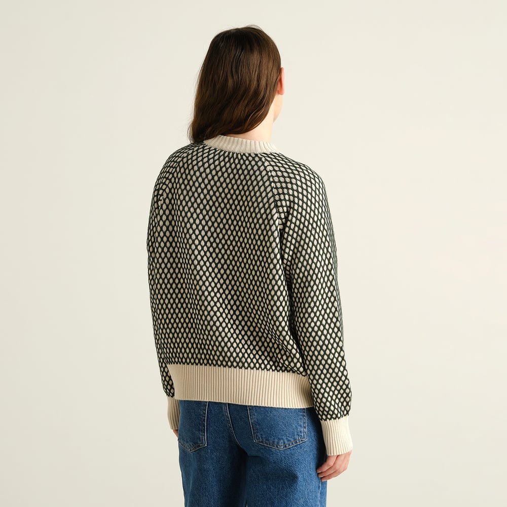 Bakifrån av en modell som bär den mönstrade tröjan Husie Bubble Knit i mörkgrönt och vaniljvitt med blå jeans.