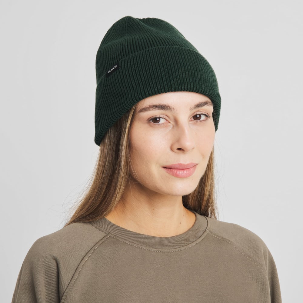 Front view of a model with long brown hair wearing the dark green, chunky-knit Beanie Hemavan.