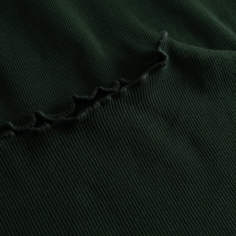 Close-up detail shot of the Rib Dress Lofta in dark green, showing the soft ribbed fabric and delicate lettuce seam.