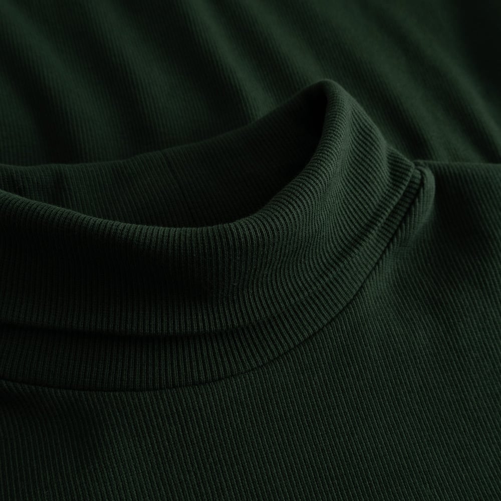 A detailed close-up of the Rib Top Malma in dark green, showing the soft ribbed texture and cozy turtleneck collar.