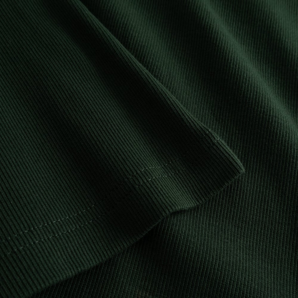 A close-up shot of the rich dark green ribbed fabric and sleeve hem detail of the Malma Top.