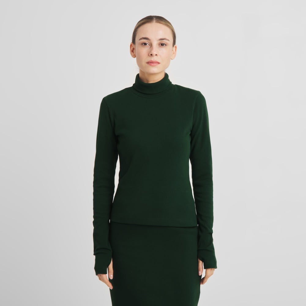 Front view of a model wearing the dark green Rib Top Malma, a slim turtleneck with long sleeves featuring thumbholes.