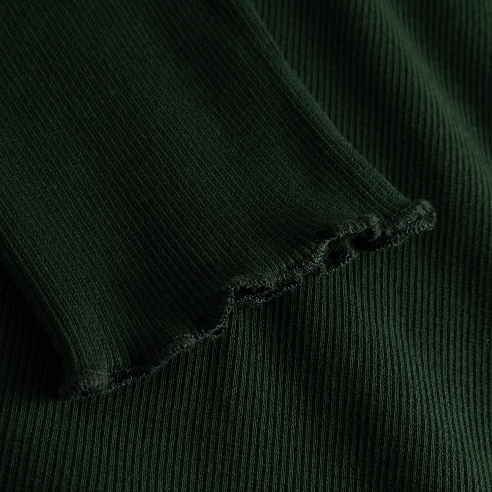 Close-up of the Rib Top Ryd in dark green, showing the detailed lettuce seam and soft ribbed fabric on the sleeve cuff.