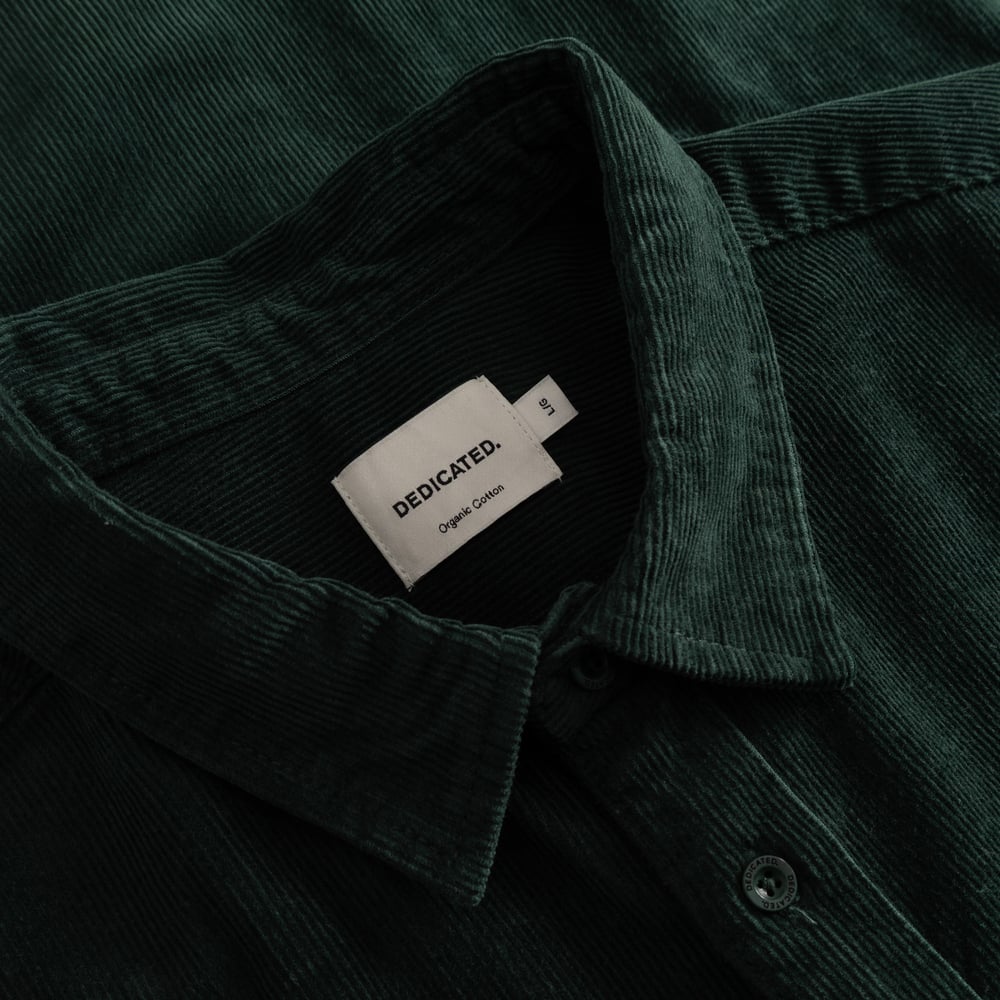 A close-up studio shot of the Dedicated brand label inside the collar of the dark green corduroy shirt Varberg.