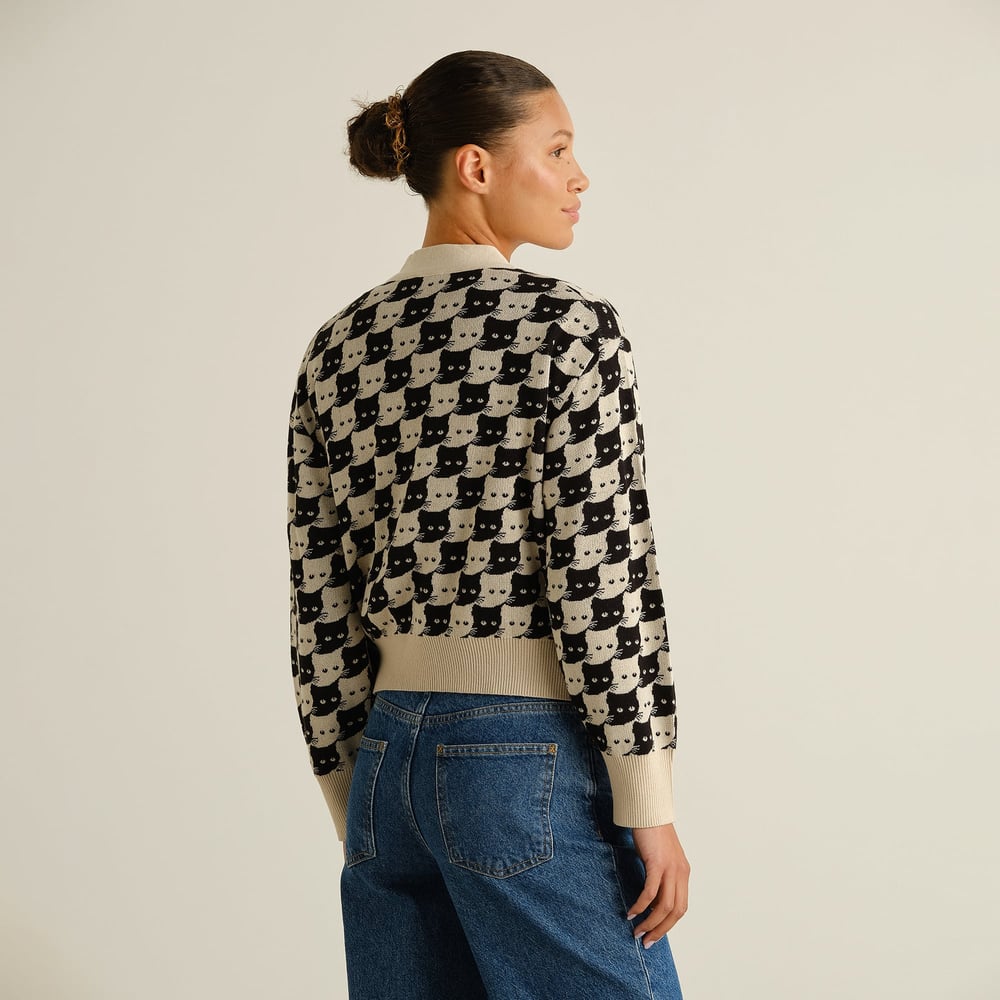 Woman seen from behind wearing the fun Kanan Cardigan with its all-over cat pattern, paired with classic blue jeans.