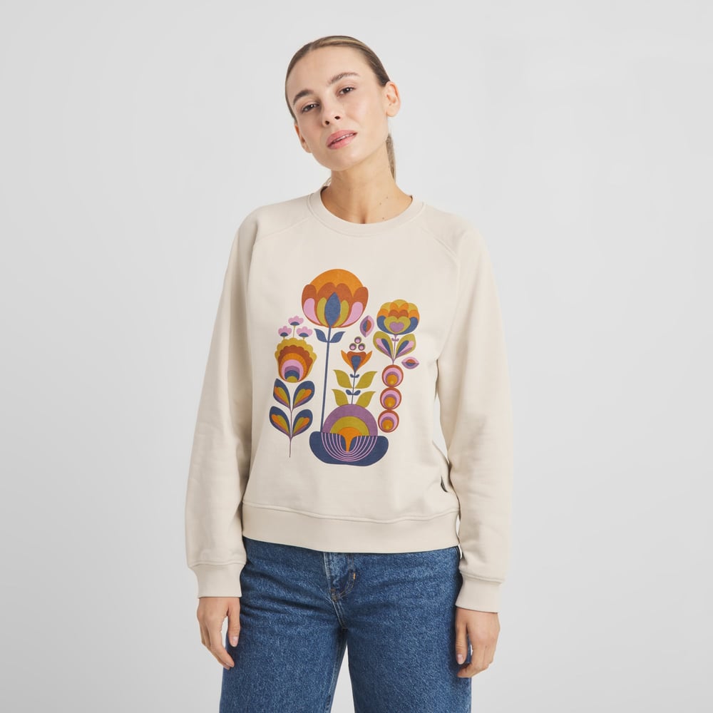 A model wears the oat white Ystad sweatshirt, featuring a vibrant, retro-inspired 'Autumn Harvest' floral graphic.