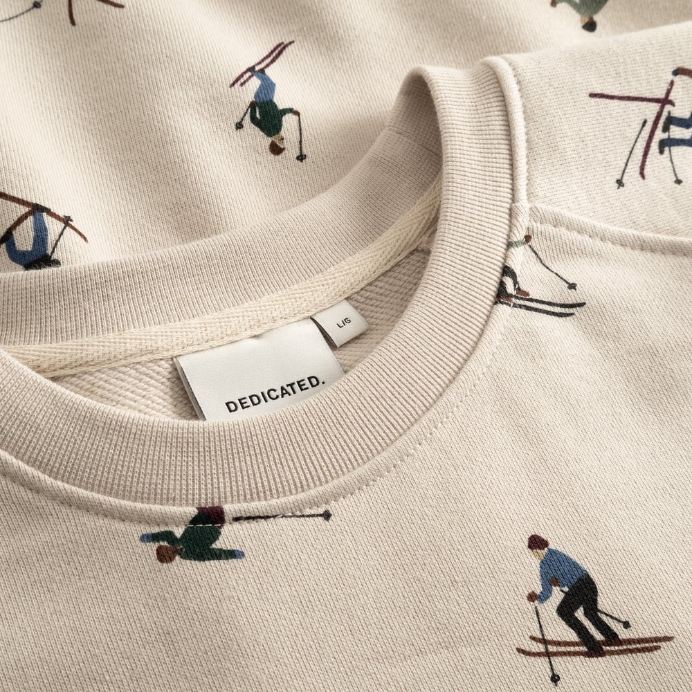 Close-up of the oat white Malmoe Ski Team sweatshirt's ribbed neckline, showing the all-over print of tiny colourful skiers.