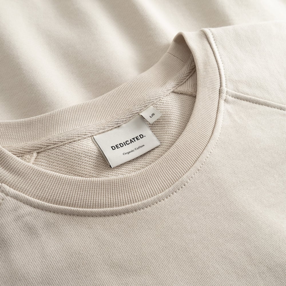 Close-up detail of the Sweatshirt Malmoe Ski Crash in Oat White, showing the ribbed collar and the Dedicated brand label.