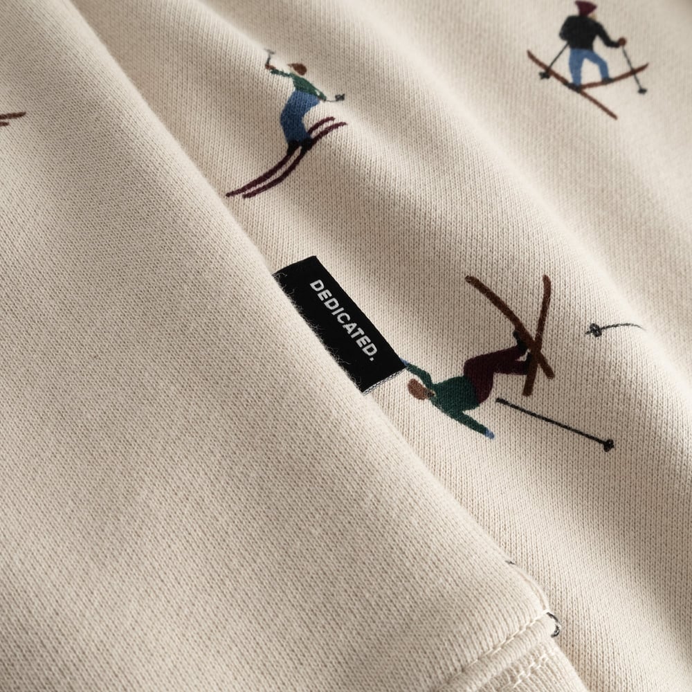 Close-up of the oat white Hoodie Falun Ski Team, featuring the all-over skier print and the black Dedicated brand tag.