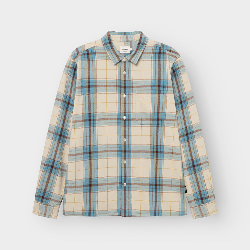 Photo de studio de la chemise Rute en flanelle à carreaux tartan blanc avoine, bleu et brun, à plat sur fond gris clair.