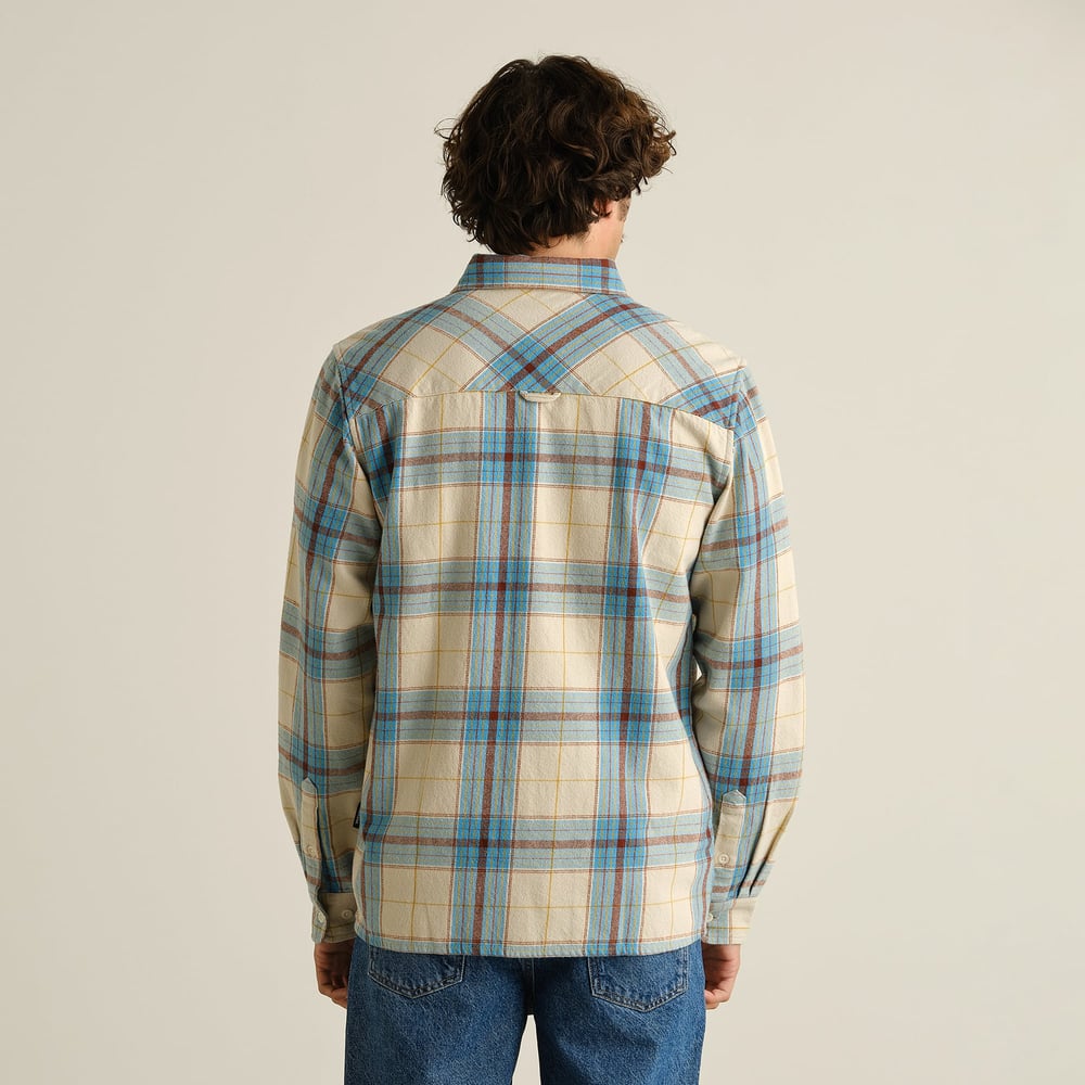 Modèle de dos portant la chemise en flanelle Rute coupe décontractée à carreaux tartan bleus et marrons et jean bleu.