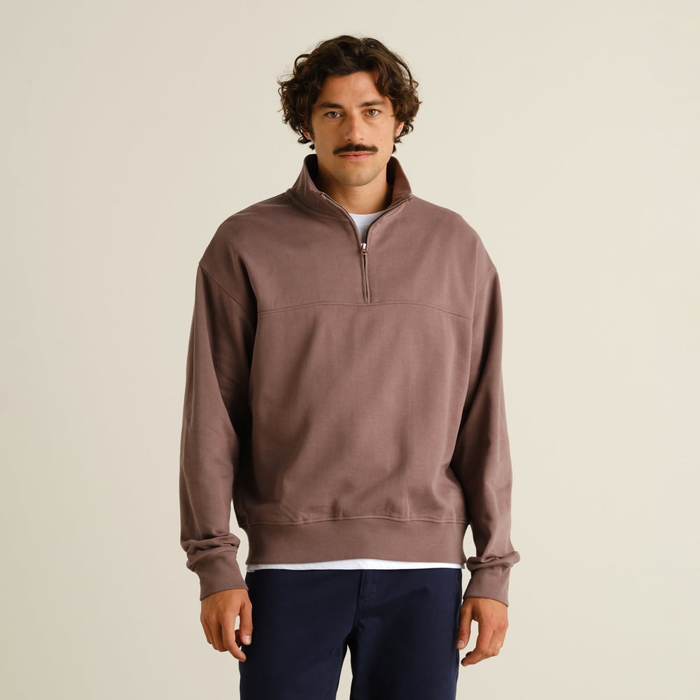 A man looks at the camera while wearing the relaxed-fit Half Zip Sweatshirt Sandvalla in Sparrow Brown.