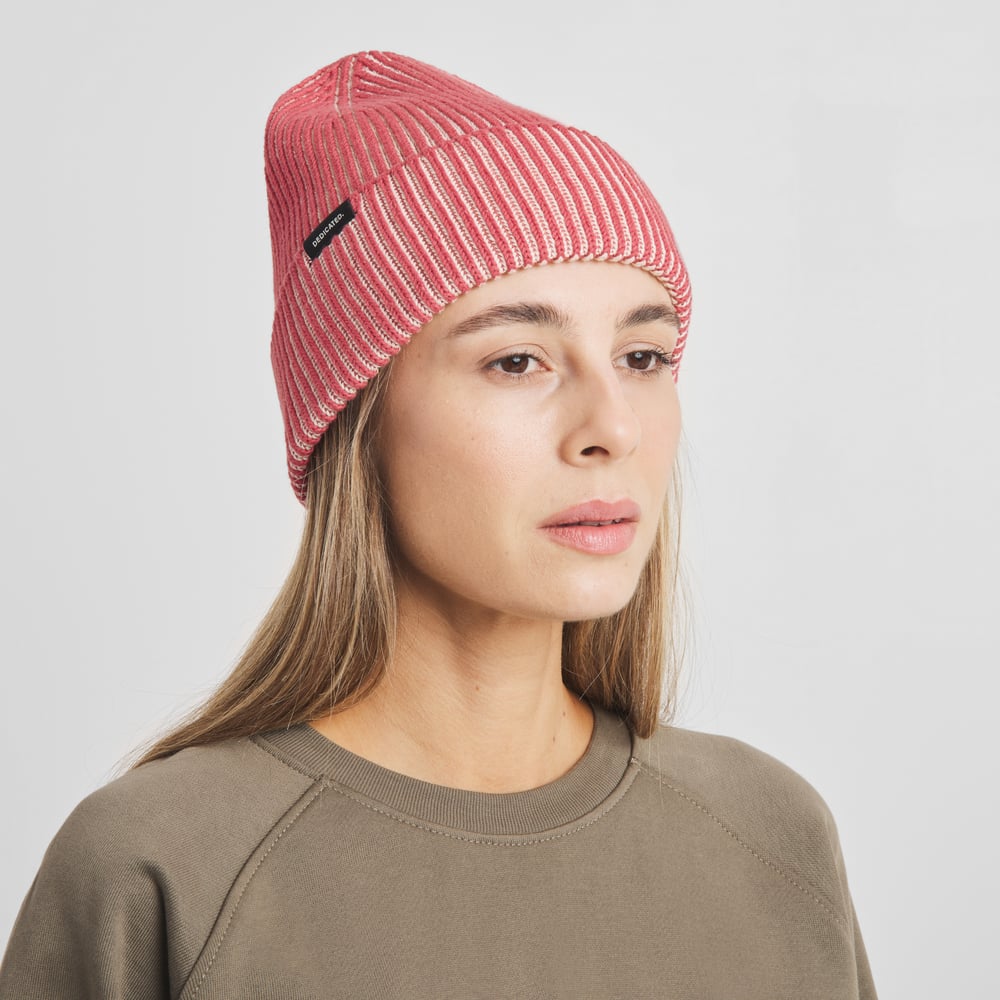 En kvinna med en fundersam blick bär den grovstickade mössan Hemavan i Vanilla White/Holly Red.
