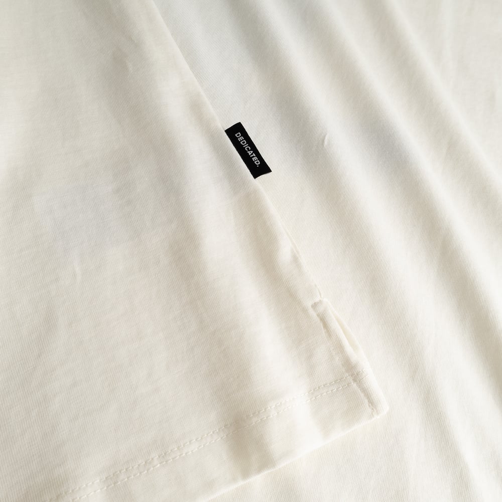 Close-up of the off-white T-shirt Visby, showing the organic cotton fabric, side slit, and a small Dedicated brand tab.