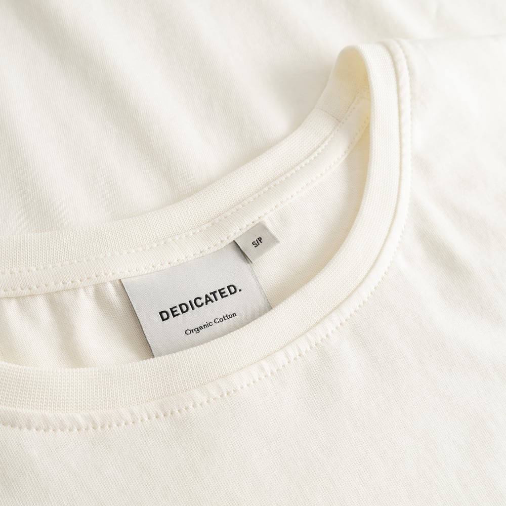 Close-up of the neckline and brand label on the T-shirt Visby Watercolor Cat in off-white organic cotton.