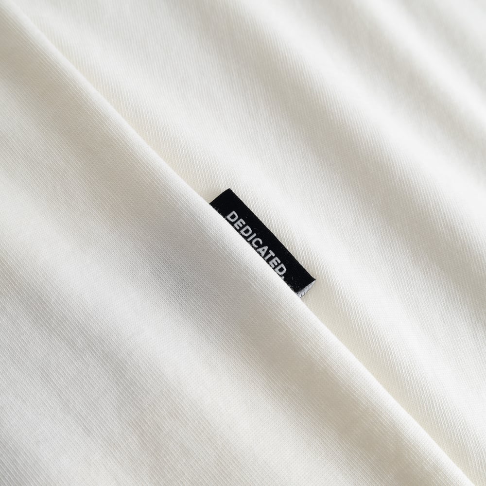 Close-up of the Dedicated brand label on the side of the soft, off-white T-shirt Stockholm Painted Side Bike.