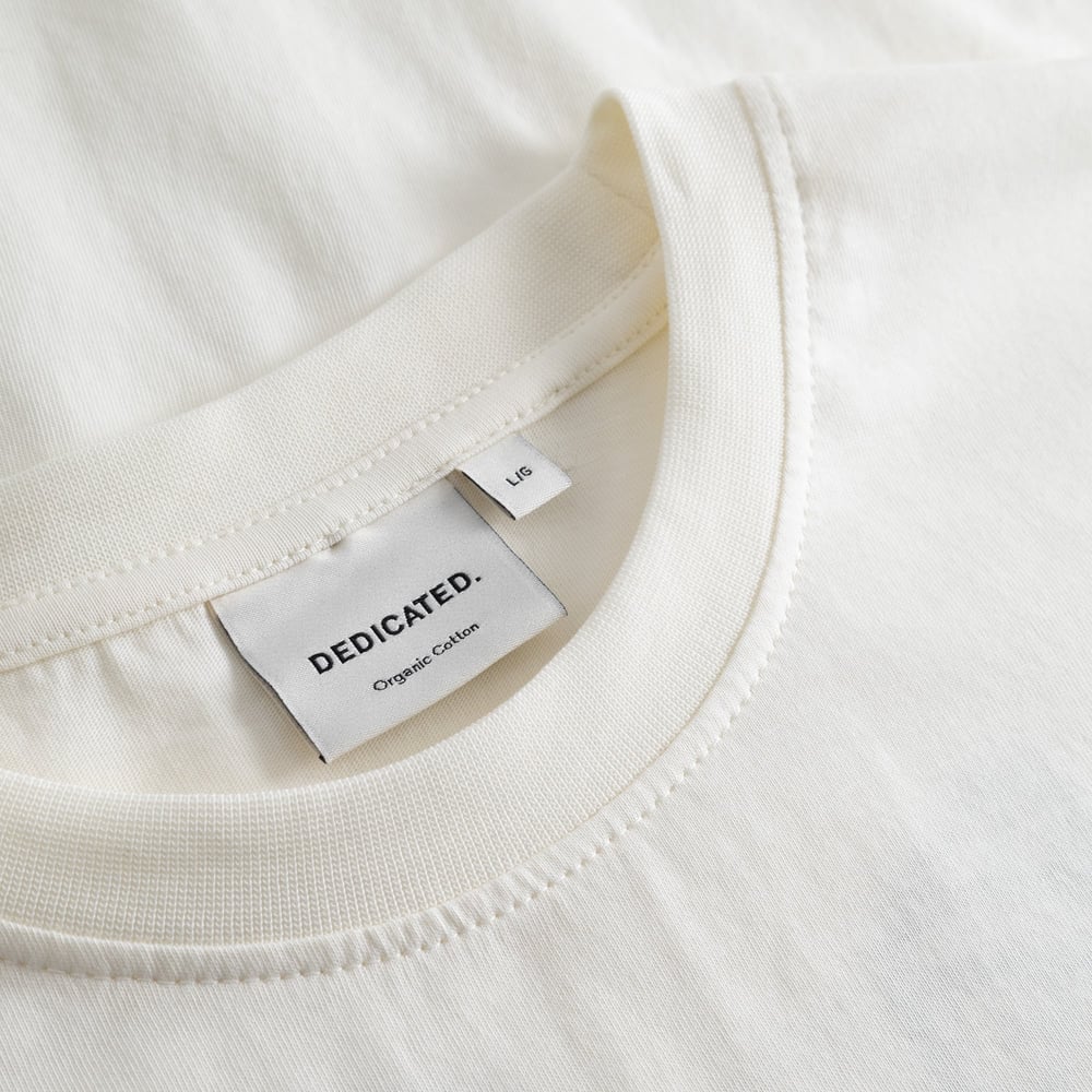 A detailed close-up of the ribbed crew neck and brand label on the off-white T-shirt Stockholm Camp Crew.