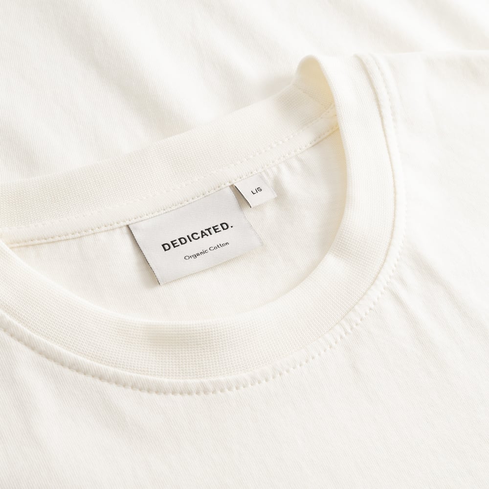 Close-up detail of the Dedicated brand label and ribbed collar on the T-shirt Stockholm Spilled Off-White.